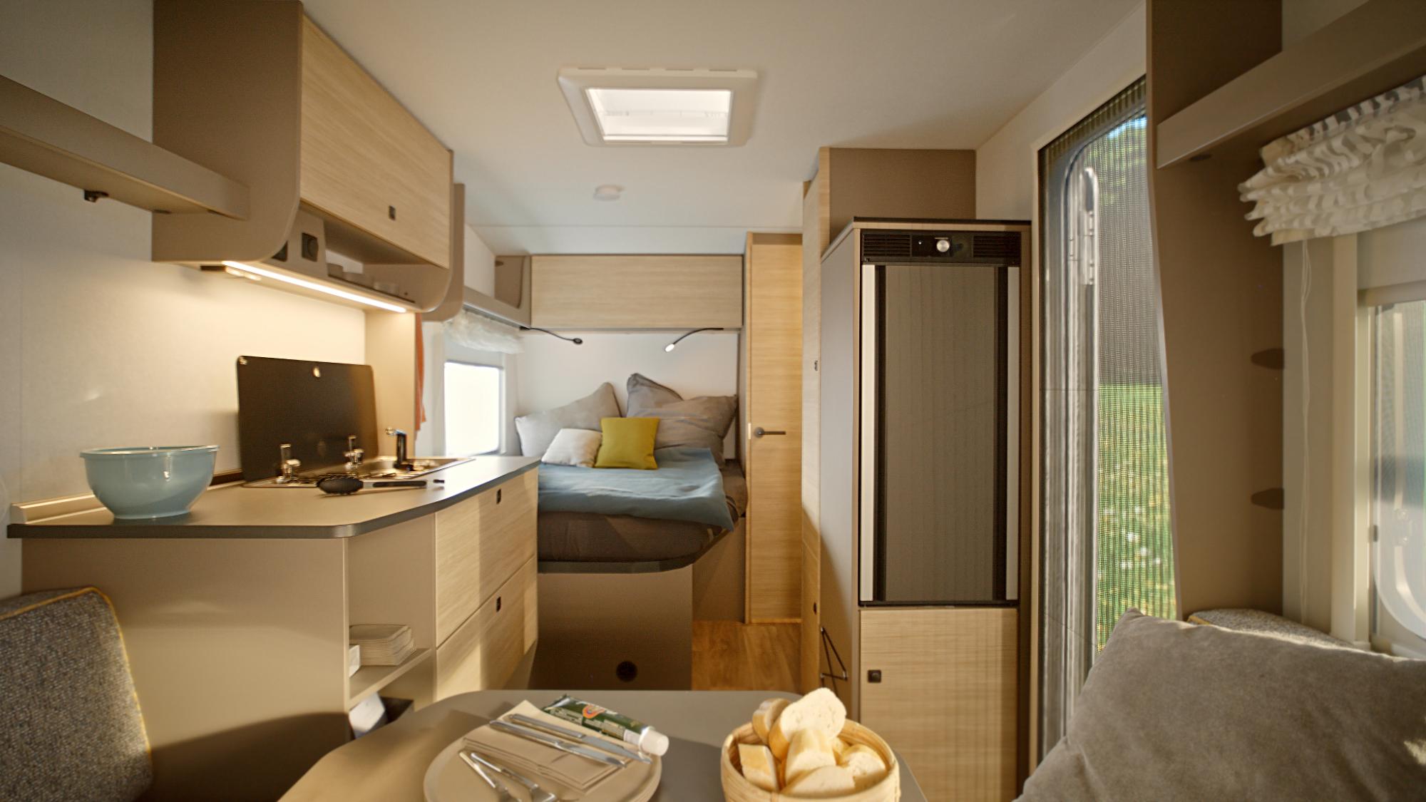 Moderner Innenraum des NEXT Caravan mit heller Holzhaptik, gemütlichem Festbett, Küchenzeile und Blick ins Grüne