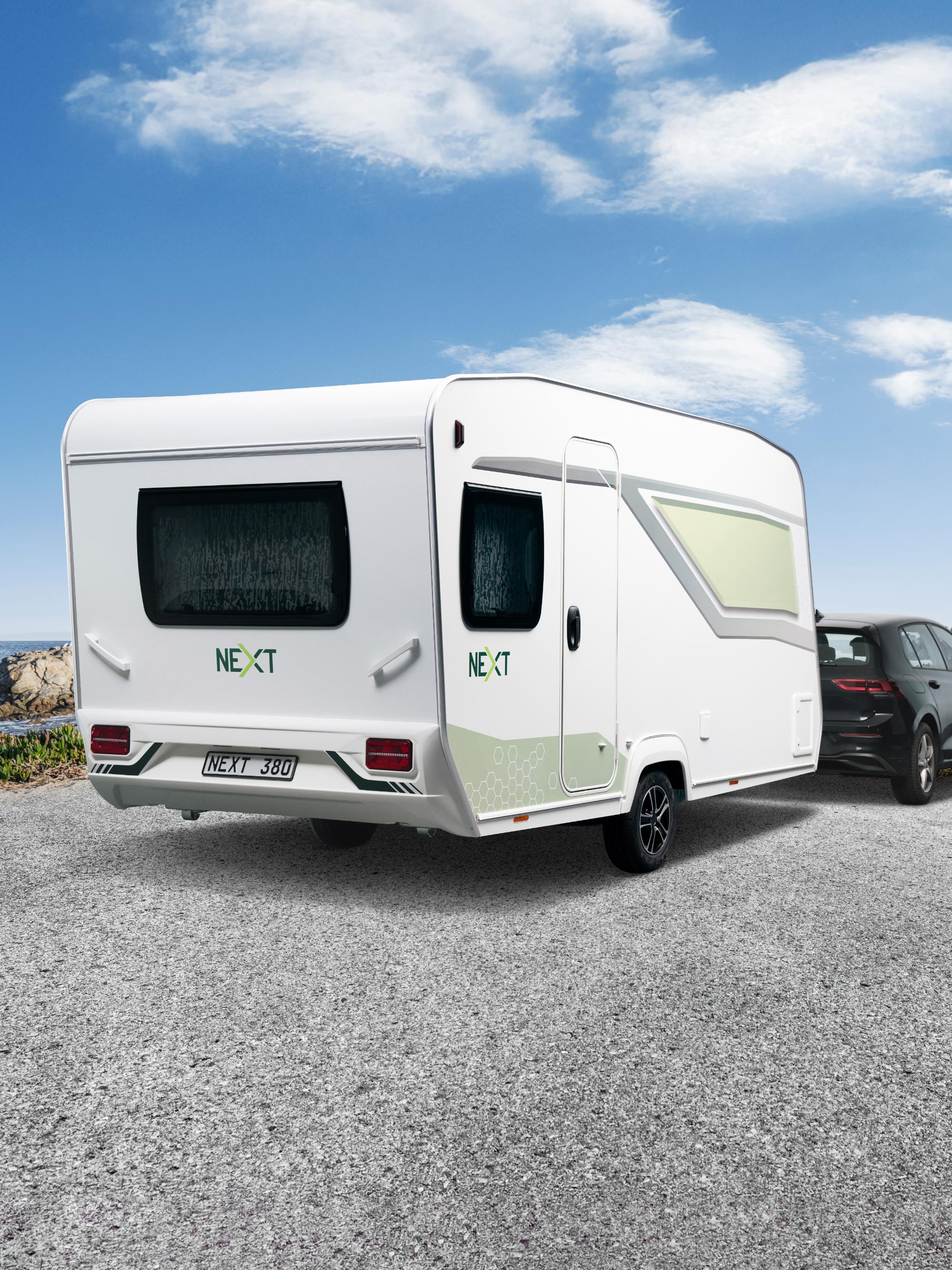 Weißer NEXT 380 Caravan mit modernem Wabendesign in der Heckansicht vor einer Küstenlandschaft mit blauem Himmel und Meer